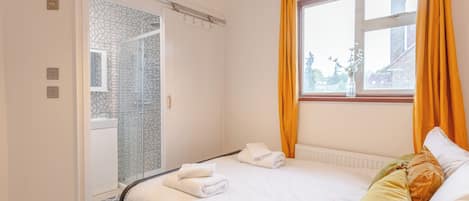 A hotel room with a bed, a window with curtains, a radiator, and a shower area.