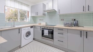 Eine kleine Küche mit Waschmaschine, Backofen und einem Fenster mit Jalousien.
