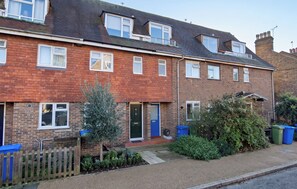 A two-story brick terraced house with a front garden, a small tree, and a blue door. - Central 3BD House With Garden - 4min walk to Tube! (London)