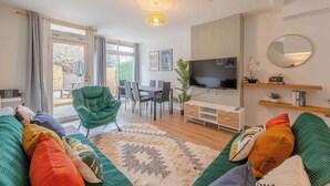 Ein modernes Wohnzimmer mit einer Couch, einem grünen Sessel, einem Fernseher und einem Essbereich mit Stühlen und einem Tisch.