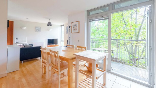 A modern kitchen with a dining area, large windows, and a balcony with a view of trees. - Spacious 2BDR Flat in the Heart of West London (London)