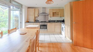 A modern kitchen with wooden cabinets, a dining table, and a large window. - Spacious 2BDR Flat in the Heart of West London (London)