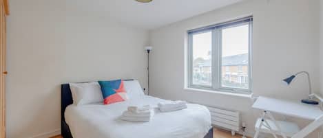 A bedroom with a bed, a desk, a chair, a window, and a ceiling light.