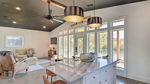 A modern kitchen with a large island, pendant lights, and a view of a lake. - Modern Norfork House w/ Patio on White River! (Norfork)