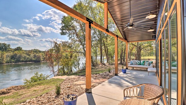 A covered outdoor area with a view of a lake, wooden beams, and a seating area with cushions. - Modern Norfork House w/ Patio on White River! (Norfork)