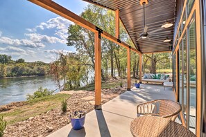 Un espacio al aire libre cubierto con vistas a un lago, vigas de madera y una zona de estar con cojines.