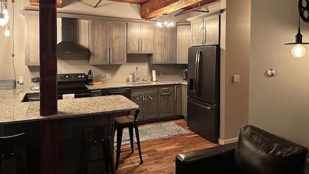 A modern kitchen with granite countertops, wooden cabinets, and a black refrigerator. - Okemo Condo on Bus Route in Center of Town (Ludlow)
