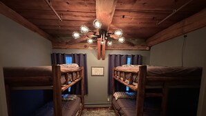 A bunk room with wooden bunk beds, a ceiling light fixture, and a rug on the floor. - Okemo Condo on Bus Route in Center of Town (Ludlow)