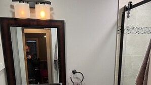 A bathroom with a wooden vanity, a white sink, a mirror, a toilet, and a glass shower enclosure. - Okemo Condo on Bus Route in Center of Town (Ludlow)