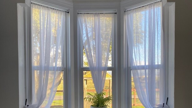 A bay window with sheer white curtains, a small wooden stool, and a potted plant. -  1887 large Ferndale Farmhouse with amazing views! Completely updated. (Ferndale)