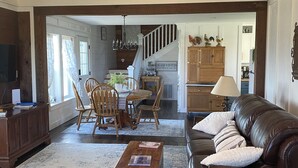A spacious living room with a brown leather sofa, a wooden coffee table, and a dining area with a wooden table and chairs. A staircase leads to the kitchen area in the background. -  1887 large Ferndale Farmhouse with amazing views! Completely updated. (Ferndale)