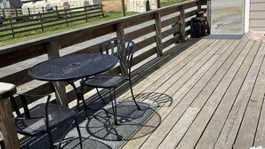 A wooden deck with metal tables and chairs, a flower pot with red and white flowers, and a covered area in the background. -  1887 large Ferndale Farmhouse with amazing views! Completely updated. (Ferndale)
