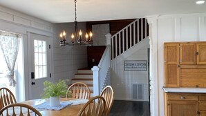 A dining area with a wooden table and chairs, a chandelier, and a staircase leading to a kitchen. -  1887 large Ferndale Farmhouse with amazing views! Completely updated. (Ferndale)