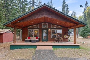 Una cabaña de madera con porche cubierto, ventanas amplias y mobiliario de exterior.