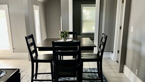 Un comedor con una mesa rectangular, cuatro sillas, un tapete y una planta en maceta.