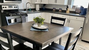 Una cocina moderna con armarios blancos, un microondas de acero inoxidable, una estufa a gas y una cafetera.