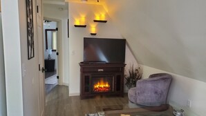 A living room with a fireplace, a flat-screen TV, a purple armchair, and a glass coffee table. - Views of the Mountain from the private decks of this upstairs condo. (Pinehurst)