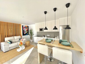 A modern kitchen with white cabinets, black pendant lights, and a dining area with a wooden table and white chairs.