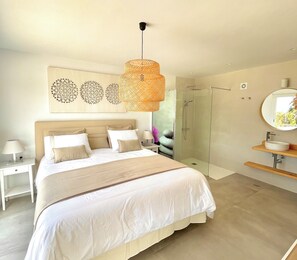 Ein Schlafzimmer mit einem großen Bett, einem Nachttisch, einer Stehlampe, einer Dusche und einem runden Spiegel.
