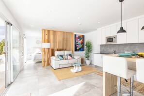 Una cocina moderna con armarios blancos, un separador de madera y un comedor con un taburete de bar.