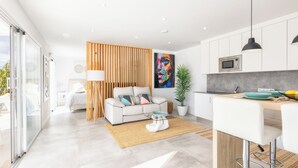 A modern kitchen with white cabinets, a wooden partition, and a dining area with a bar stool. - TAJUYA SUITE (Los Llanos)