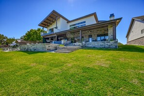 A modern two-story house with a stone facade, a covered patio, and a grassy lawn.