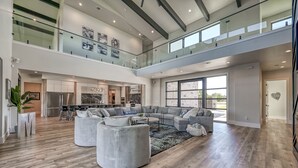 Een ruime woonkamer met een grote hoekbank, een salontafel en een glazen balustrade met uitzicht op een balkon.