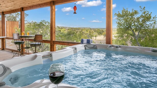 Tinaco con una copa de vino tinto, terraza de madera y zona de estar exterior con vistas al paisaje.