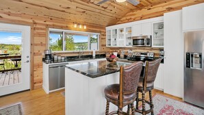 Una cocina moderna con vigas de madera, una isla central, taburetes de bar, un refrigerador y vistas al exterior.