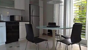 Eine moderne Küche mit weißen Schränken, einem Edelstahl-Kühlschrank und einem Glastisch mit zwei Stühlen.