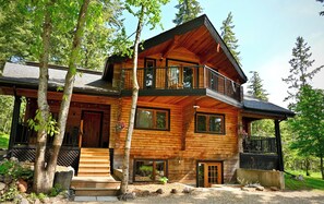 Une cabane en rondins à deux étages, dotée d’un balcon, d’une véranda et d’une pancarte de bienvenue.