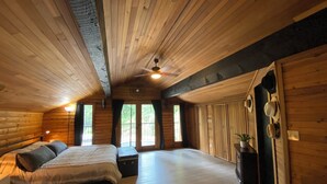 Ein Schlafzimmer in einer Blockhütte mit einem Bett, Nachttischen und einem Deckenventilator.