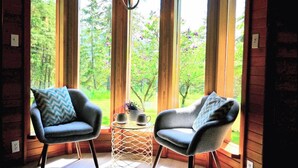 Ein Zimmer mit zwei Sesseln, die zu einem großen Fenster mit Blick auf Bäume und einer Hängelampe ausgerichtet sind.