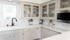 A modern kitchen with white cabinetry, a stainless steel microwave, and a window providing natural light.