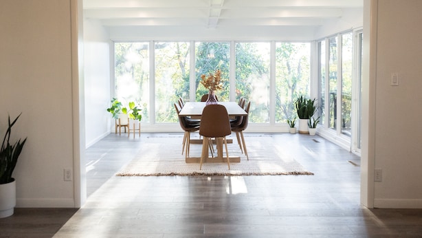 A spacious dining area with a large table and chairs, surrounded by large windows offering a view of greenery.