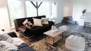 A modern living room with a black sofa, a wooden coffee table, and a patterned rug.