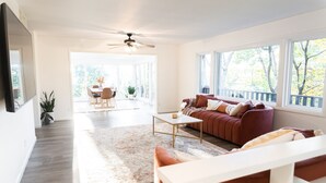 A spacious living room with a red sofa, a white coffee table, and a large window offering a view of trees.