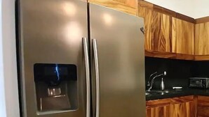 A kitchen with wooden cabinets, a stainless steel refrigerator, and a black countertop. - CONDO LI BY TRVL2HM (Cabo San Lucas)