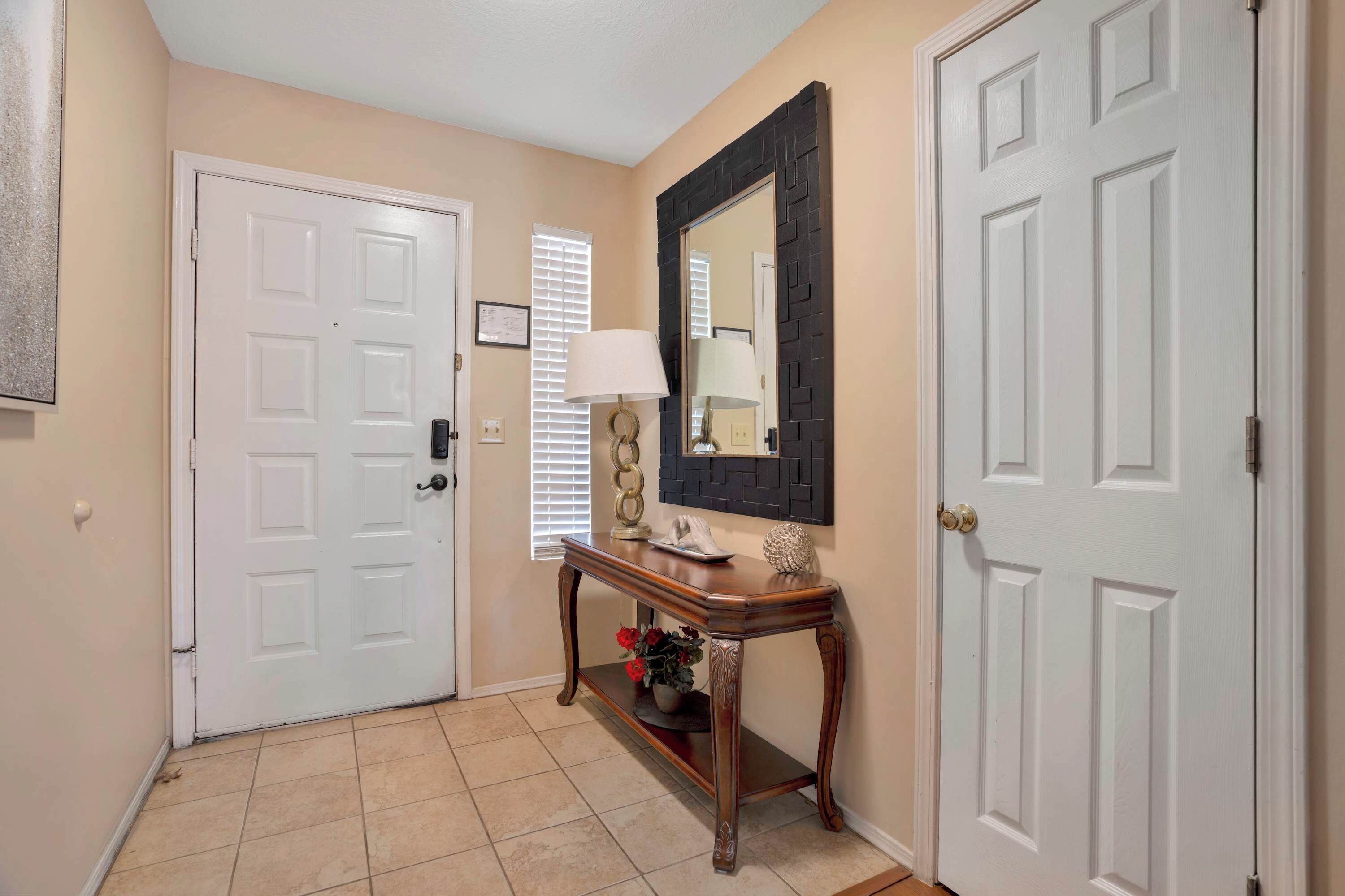 A hallway with beige walls, white doors, a wooden console table with a lamp, and a mirror.