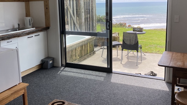 A compact room with a kitchen area, a sliding glass door leading to a patio with a view of the ocean.