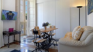 Ein Essbereich mit Holztisch und Stühlen, einem kleinen Beistelltisch mit Fernbedienung, einer Couch und einem Gemälde an der Wand.