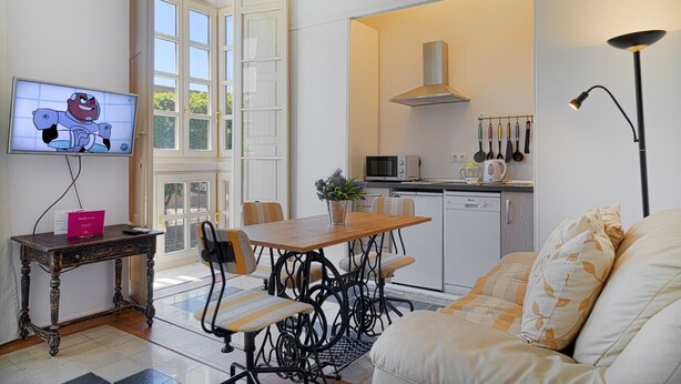 Eine moderne Küche mit Mikrowelle, Herd und hängenden Küchenutensilien. Ein Esstisch mit Stühlen steht in der Nähe eines großen Fensters.