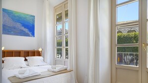 Ein Schlafzimmer mit einem Bett, einem Gemälde, einem Fenster und einer Tür.