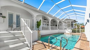 Una piscina techada con techo de cristal, barandales blancos y una escalera que lleva a una puerta con contraventanas.