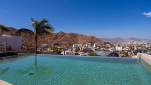 Une magnifique piscine à débordement d’un bleu profond, offrant une vue sur le paysage urbain et les montagnes en arrière-plan.