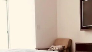 Un lit bien fait, recouvert d’une couvre-lit à motifs, dans une pièce qui ne contient qu’une seule chaise et un téléviseur fixé au mur.