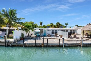 A waterfront property with a pool, lounge chairs, and a thatched-roof structure.