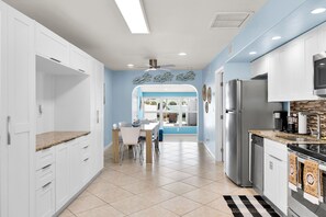 A modern kitchen with white cabinets, a stainless steel refrigerator, and a dining area with a blue wall and ceiling fan. - Adorable 2 Bedroom - Key Colony - Cabana Club - Dockage (Key Colony Beach)