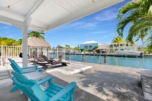 A poolside area with lounge chairs, a covered seating area, and a view of a marina with boats.