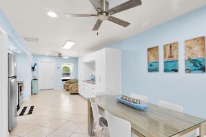 Eine moderne Küche mit Deckenventilator, ein Essbereich mit Glastisch und Wandbildern von Meereslebewesen.